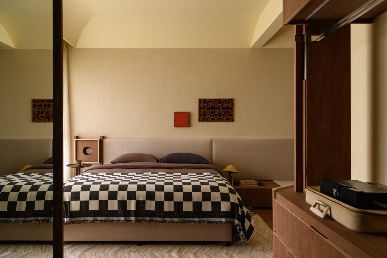 The master bedroom with a wide upholstered headboard, black and white checked bedspread, herringbone timber floor, and a pair of geometric artworks mounted above