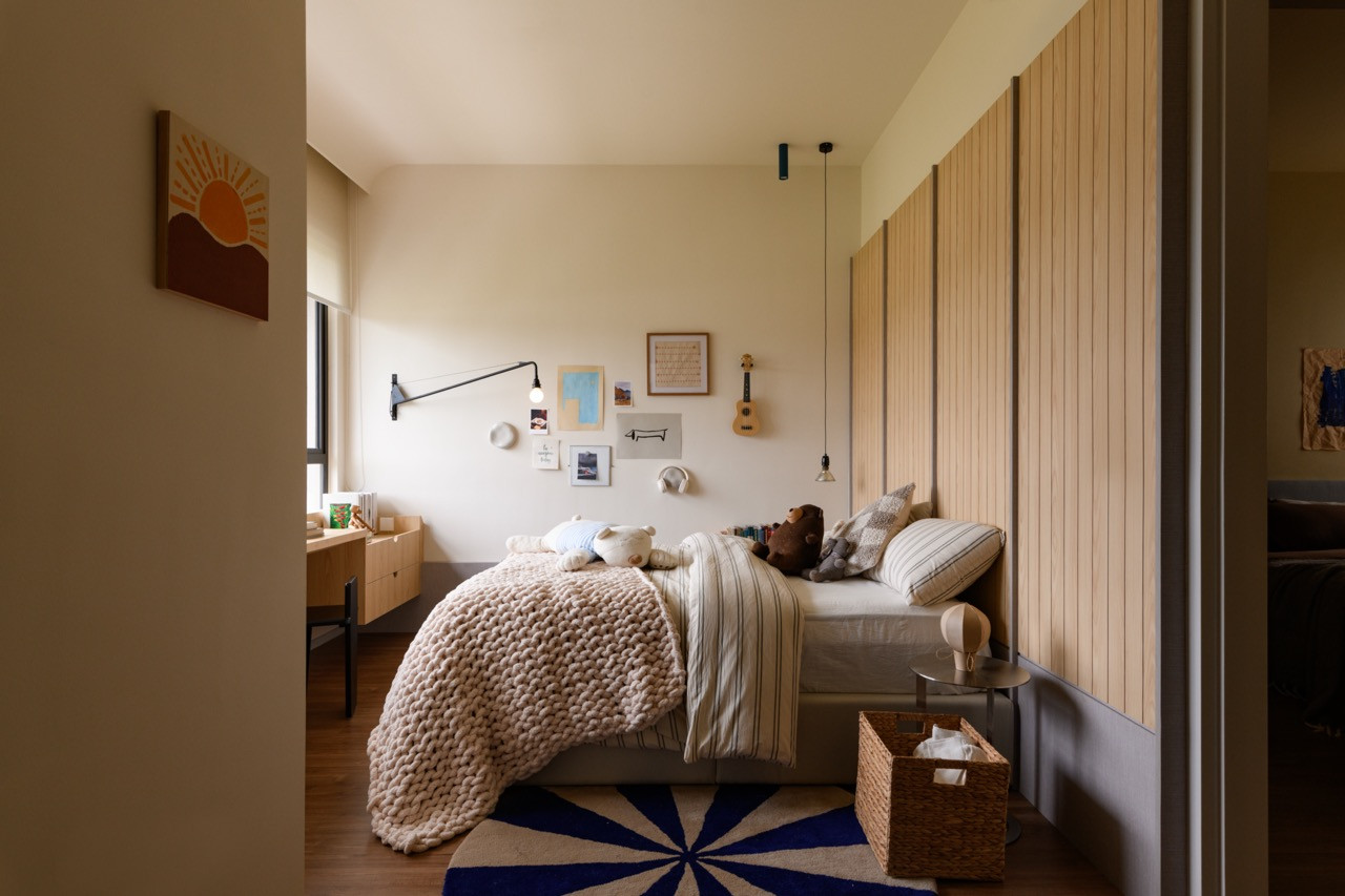 A children’s bedroom viewed from the doorway, with a vertical wood-slat wall panel, blue and white starburst rug, and a gallery wall of framed prints and personal objects