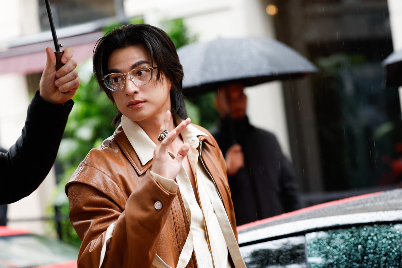 MILAN, ITALY - SEPTEMBER 27: Kanawut Traipipattanapong is seen wearing a brown leather jacket with a large, pointed collar and a zipper closure, a light-colored striped collared shirt, clear-framed glasses and a large ring, outside Ferrari fashion show during the Milan Fashion Week Womenswear Spring/Summer 2026 on September 27, 2025 in Milan, Italy. (Photo by Claudio Lavenia/Getty Images)