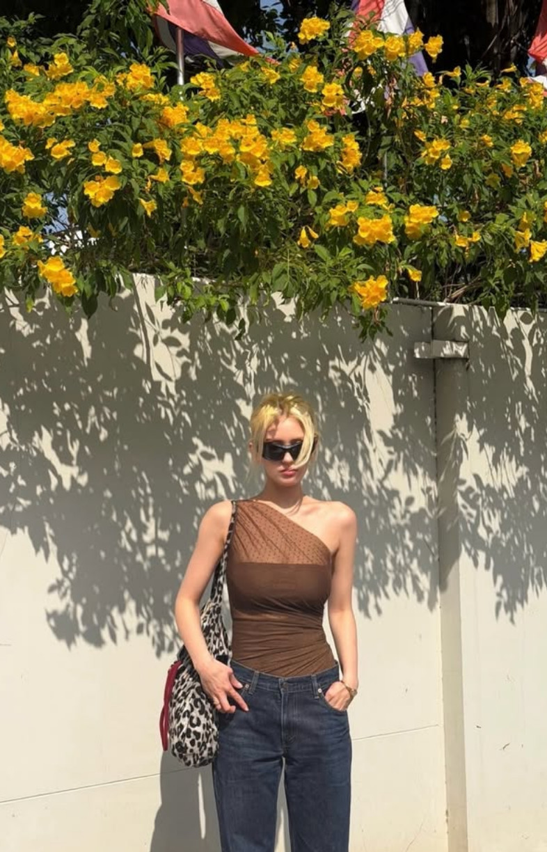 Somi in a sheer brown polka-dot one-shoulder top over a matching bandeau, paired with straight-leg denim (Photo: @somsomi0309/Instagram)