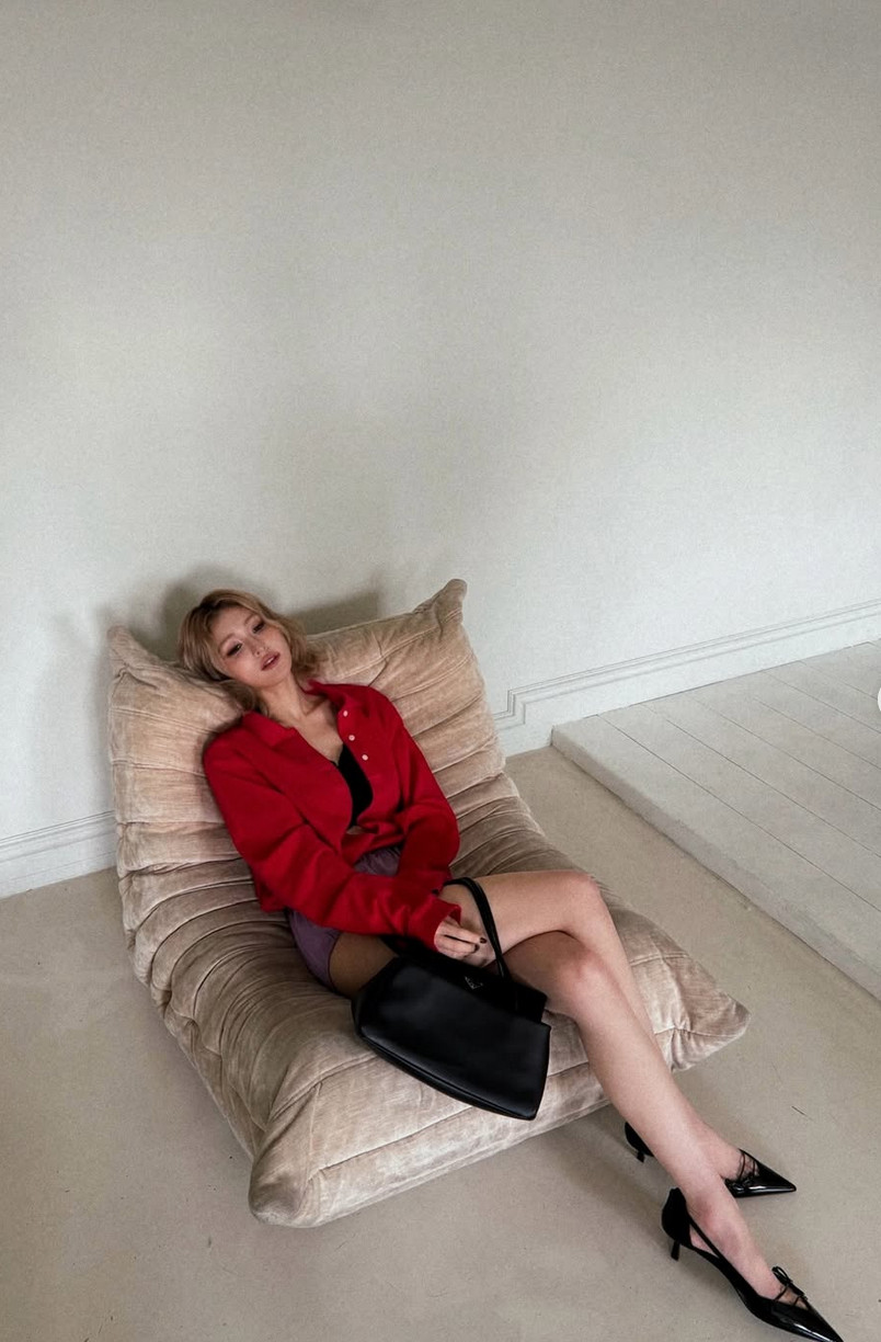 Somi lounges in a red shirt and purple mini skirt, Prada bag in hand (Photo: @somsomi0309/Instagram)