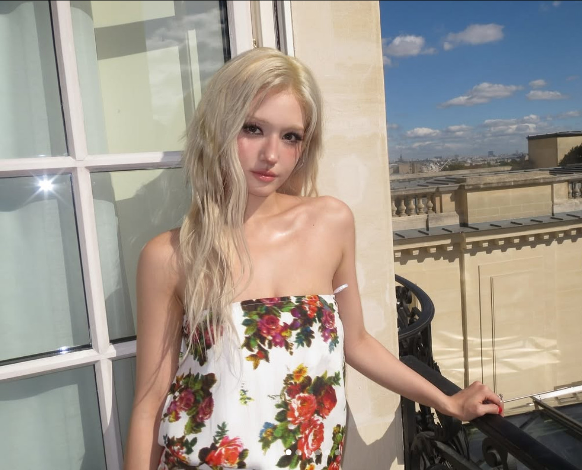Somi stands on a sunlit balcony in a white strapless dress adorned with red, pink and yellow roses (Photo: @somsomi0309/Instagram)