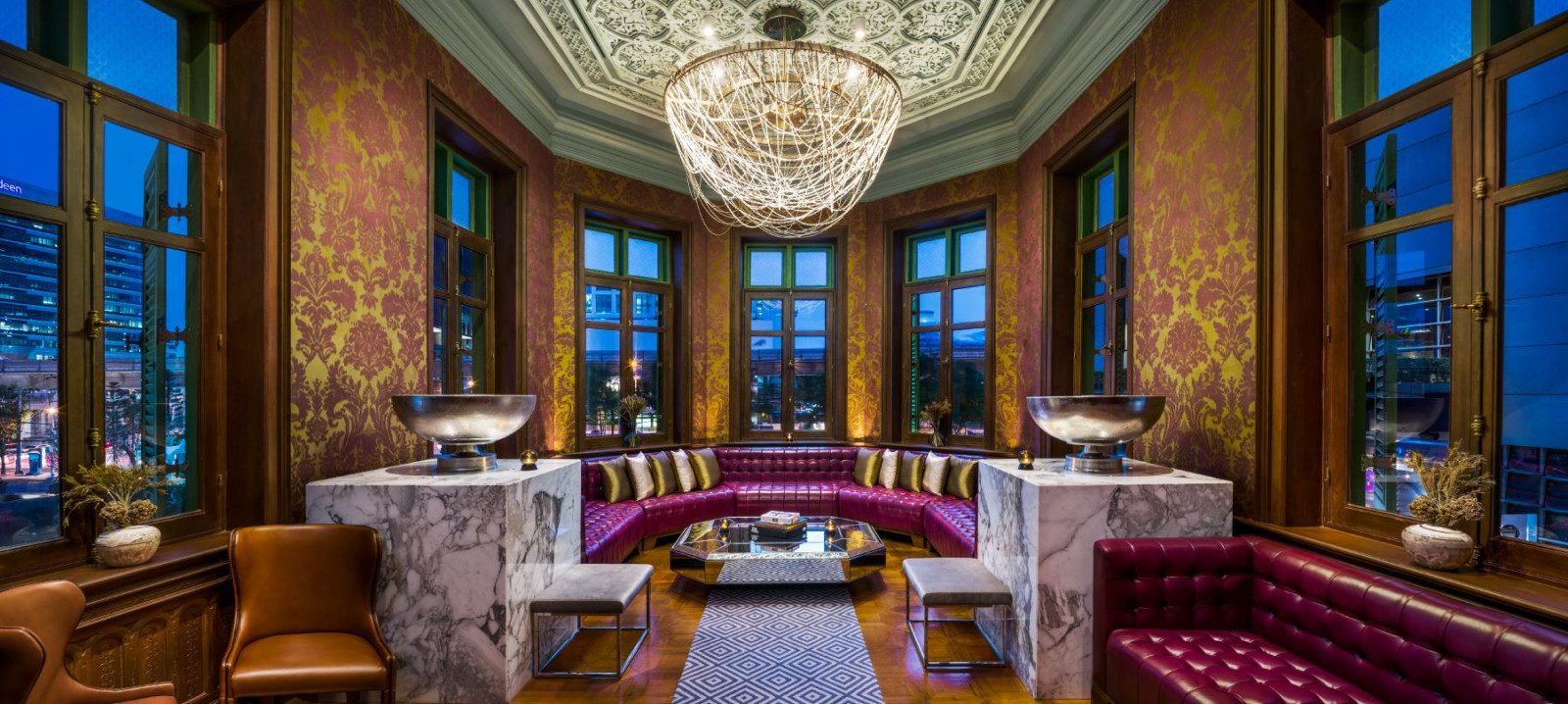 An upper-floor room at The House on Sathorn, with the original octagonal ceiling, damask wallcovering and a curved banquette set within the building’s projecting bay