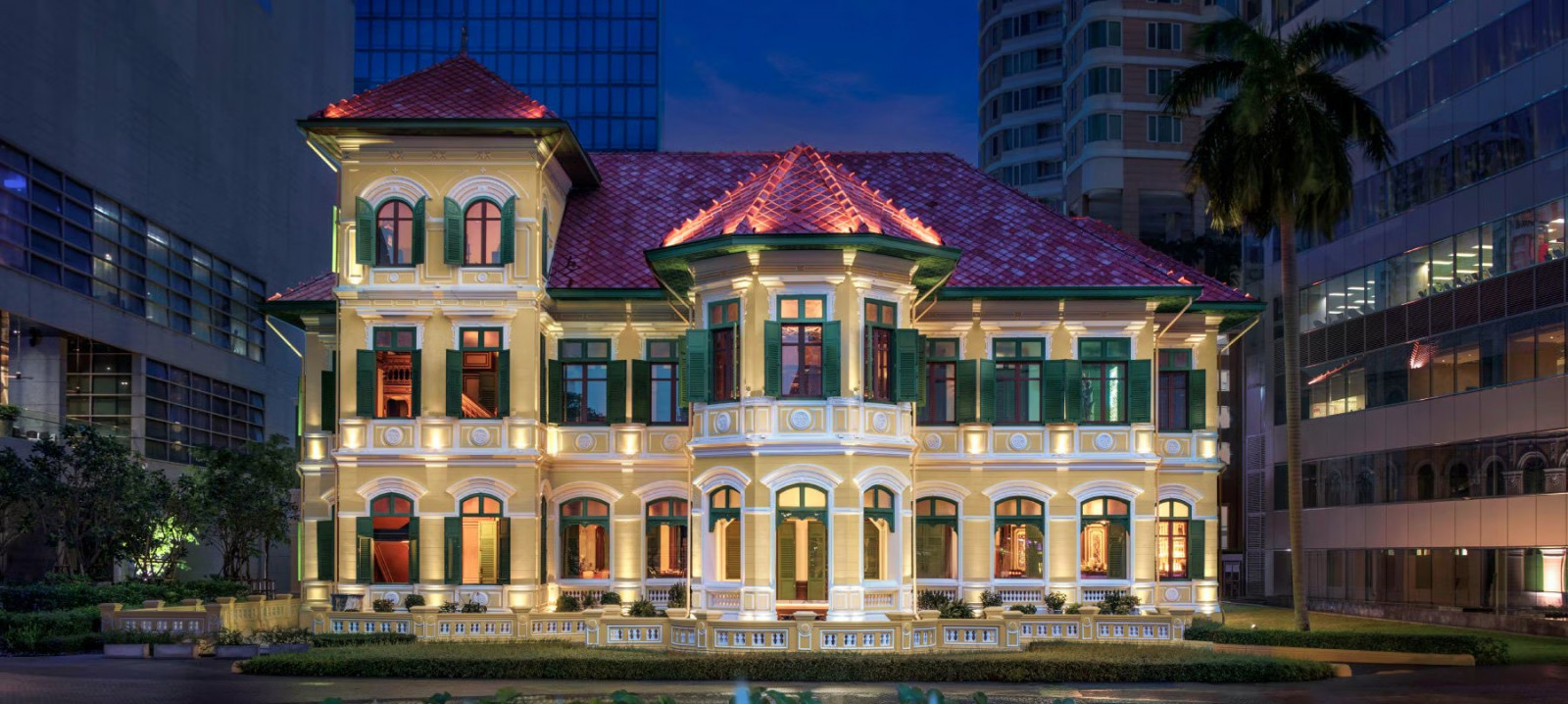 The facade of The House on Sathorn at night, the 1889 Neoclassical mansion now enclosed by the commercial towers of the Sathorn district
