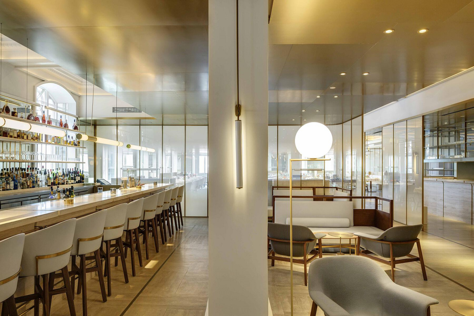The bar lounge at Jean-Georges, where Neri&Hu’s brass-framed glass volumes define the space while the original 1916 arched windows remain visible beyond