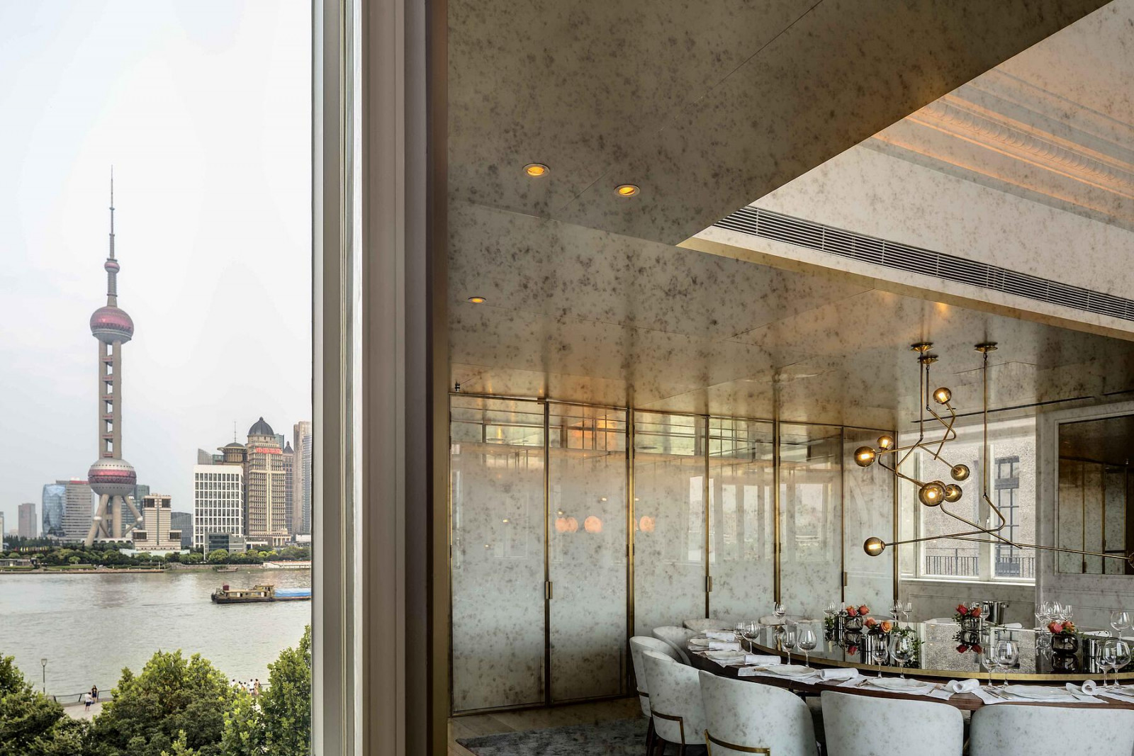 A private dining room at Jean-Georges, with Neri&Hu’s antique mirrored panels and brass detailing set against the heritage windows overlooking the Huangpu River and Pudong skyline