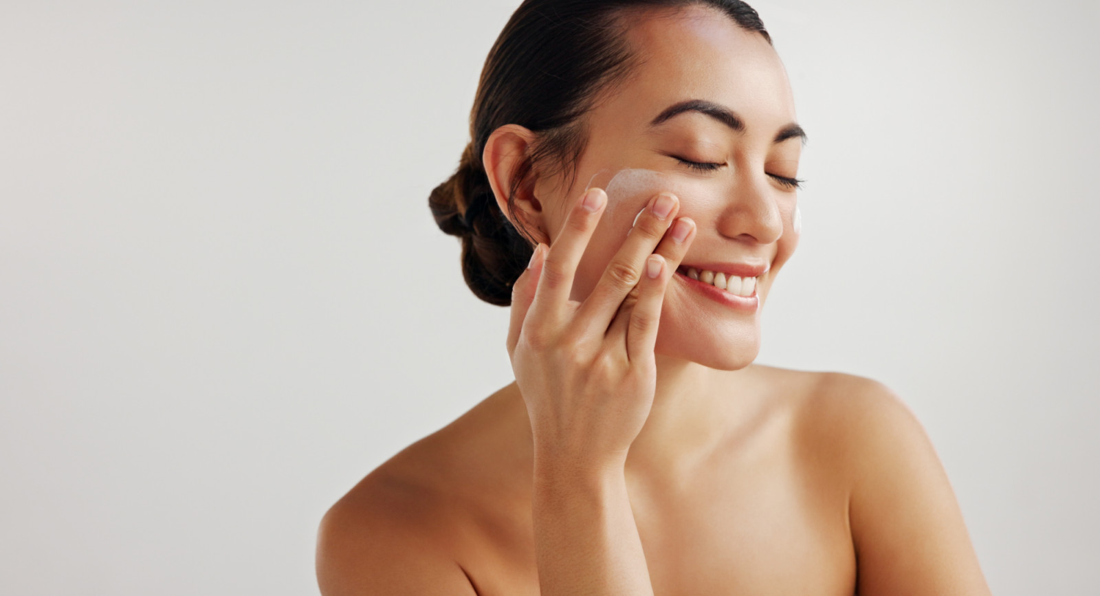 Woman, facial skin and lotion in studio for touch, happy and benefits by white background. Person, model and cosmetic cream with mock up space, beauty and serum for transformation with eyes closed