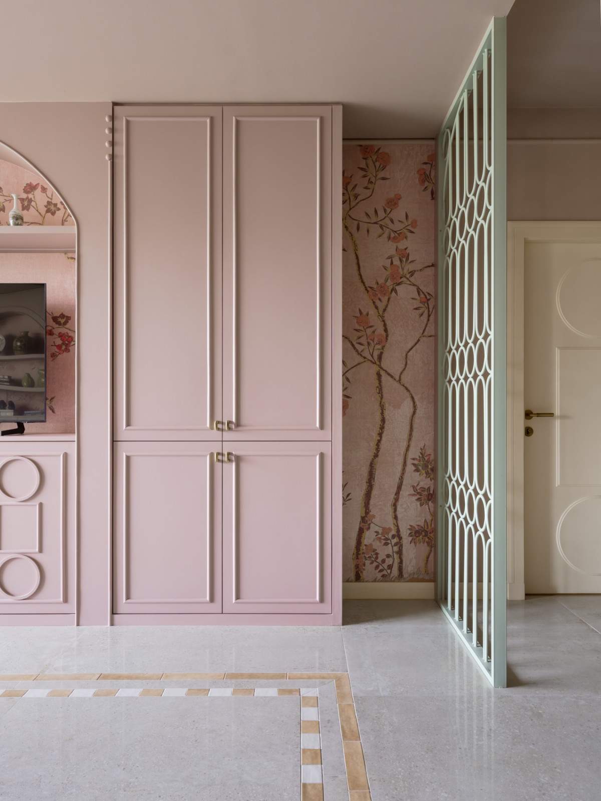 The living room wall, with dusty pink panelled cabinetry flanked by a floral chinoiserie wallpaper panel and the mint-green geometric screen partition at the edge of the frame