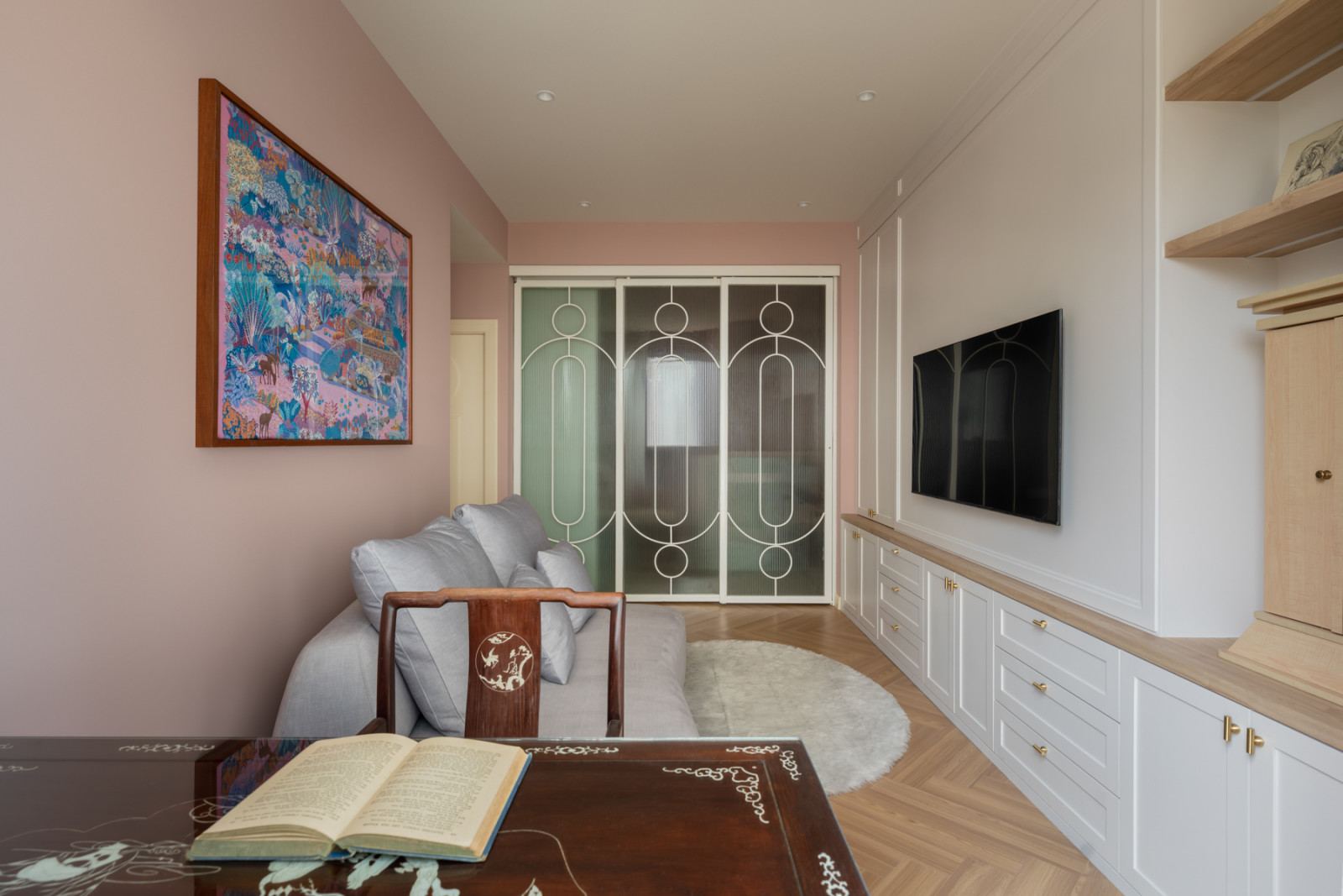 The family room, with an antique rosewood table inlaid with mother-of-pearl in the foreground, a geometric glass-and-metal sliding screen, and a large colourful artwork on the pink wall