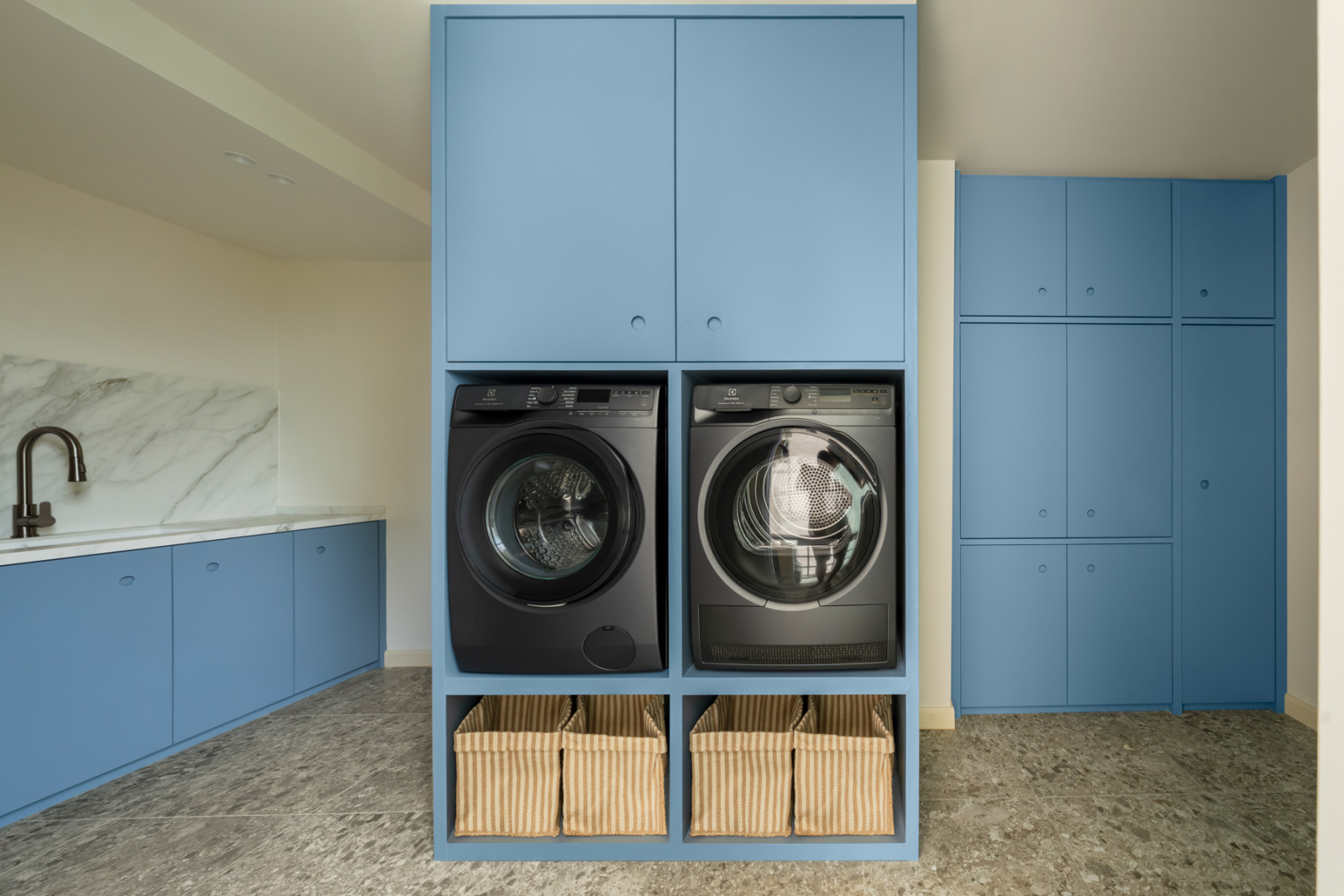 The utility room, with powder-blue cabinetry framing a side-by-side washer and dryer set into a built-in unit, woven striped laundry baskets stored below