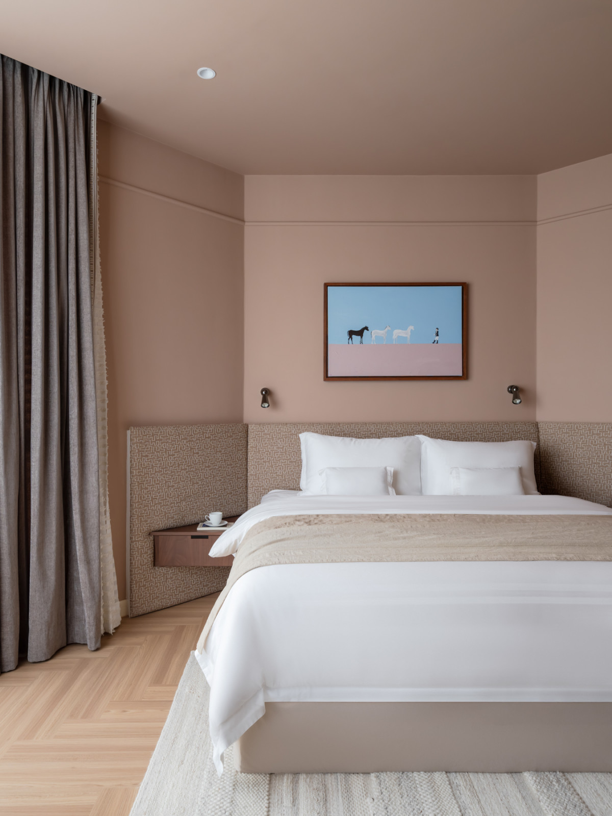 The master bedroom, with walls and ceiling in warm dusty rose, a patterned upholstered headboard, and a painting of horses and a rider hung above the bed