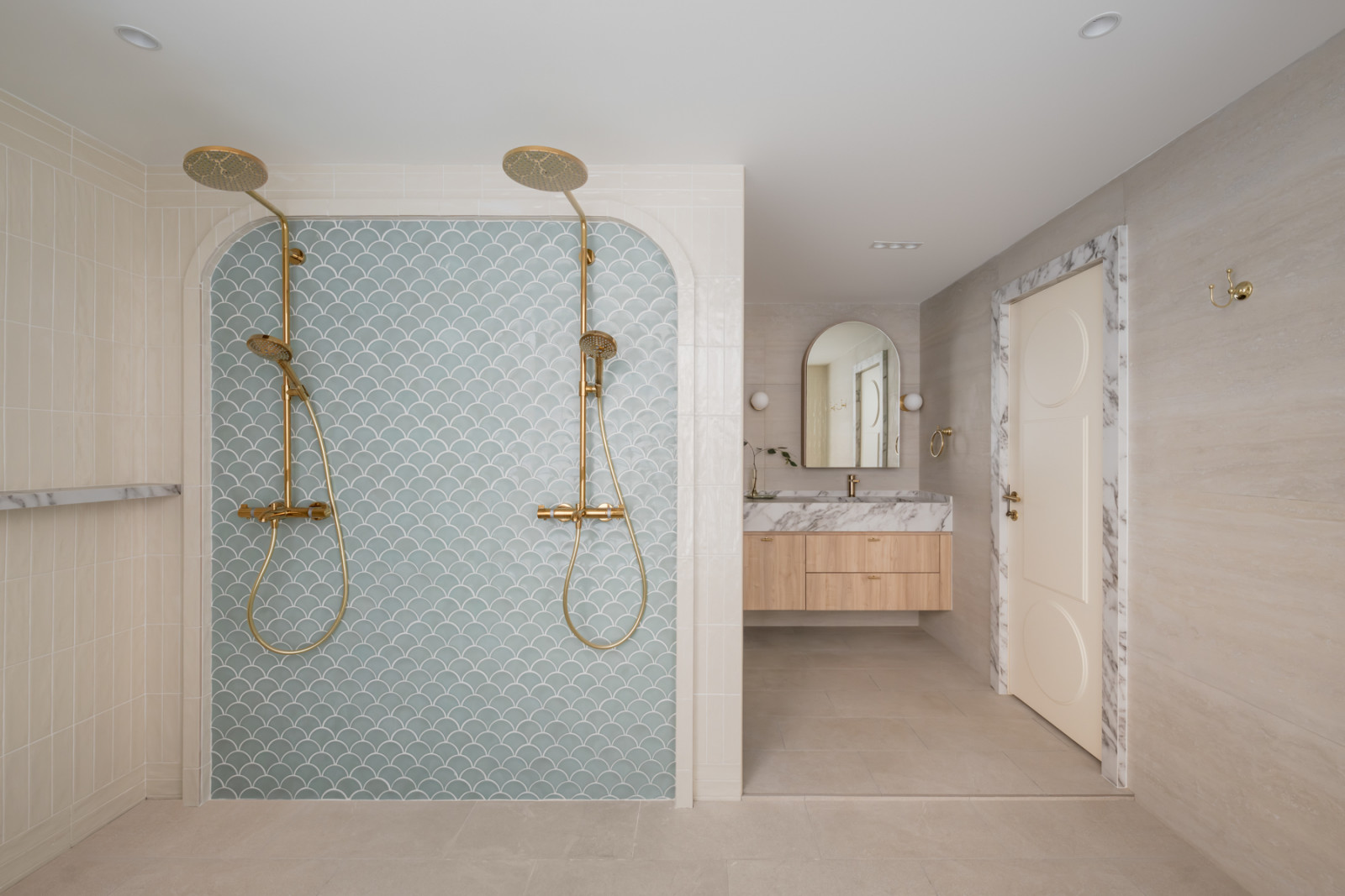 The master bathroom shower area, with fish-scale teal mosaic tiles set within a plaster arch and dual brass overhead and handheld fittings