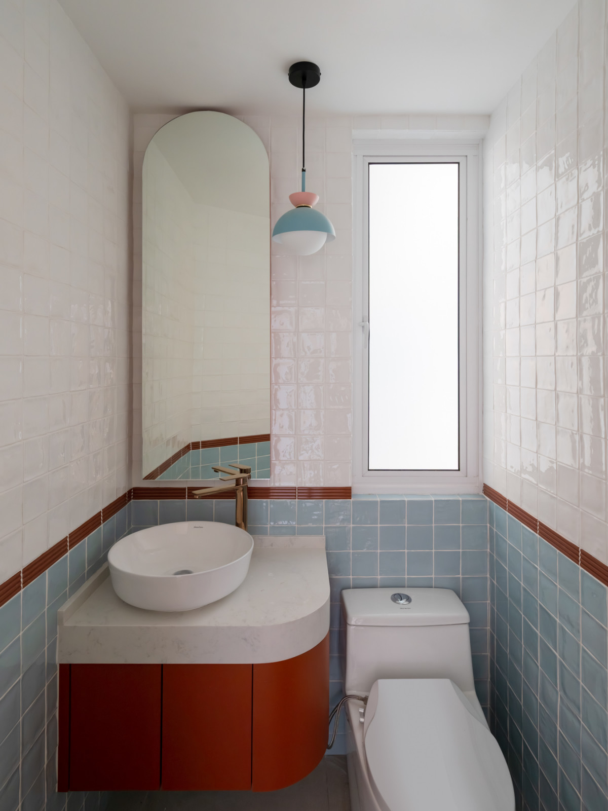 The powder room, tiled in white and duck-egg blue with terracotta pencil-line borders, a rounded floating vanity, and an arched mirror