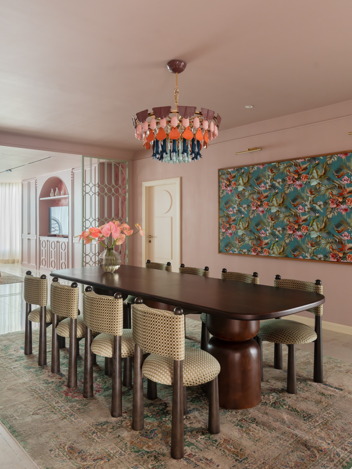 The dining room, where a Lladró ceramic porcelain chandelier in multicoloured drops hangs above the Dad’s Woods table, with a large tropical botanical artwork on the pink wall