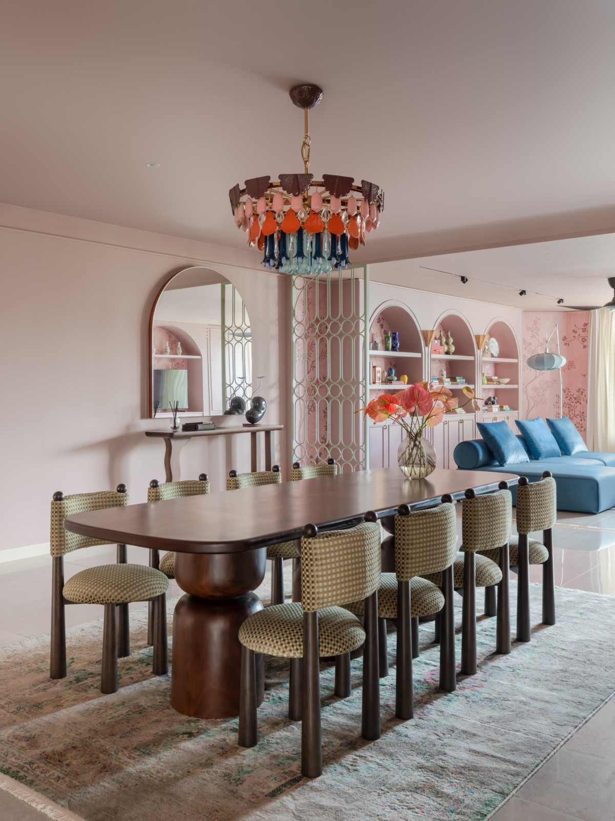 The dining and living areas in a single view, with the arched pink display shelving, the mint-green geometric screen divider, and the blue velvet sofa visible in the living room beyond