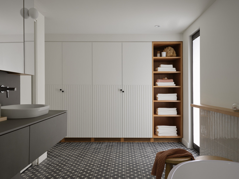 The primary bathroom has hand-painted cement tile floors, integrated timber shelving, and fluted white cabinetry