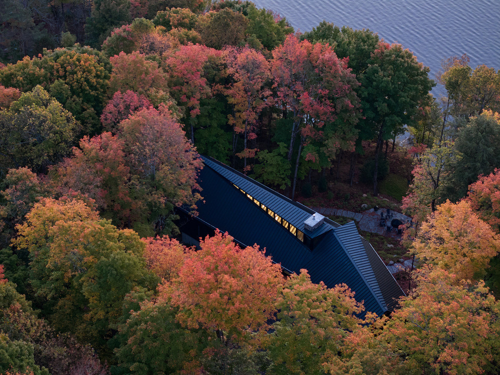An aerial view of the cottage at dusk, its single black zinc roof plane oriented parallel to the shoreline