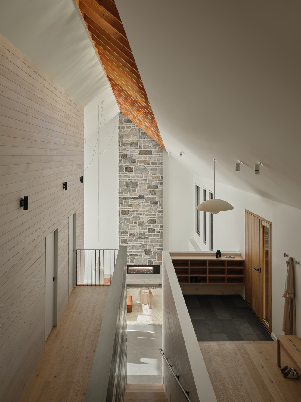 Looking down from the upper level toward the entry and mudroom below, with the stone chimney rising through the full height of the structure
