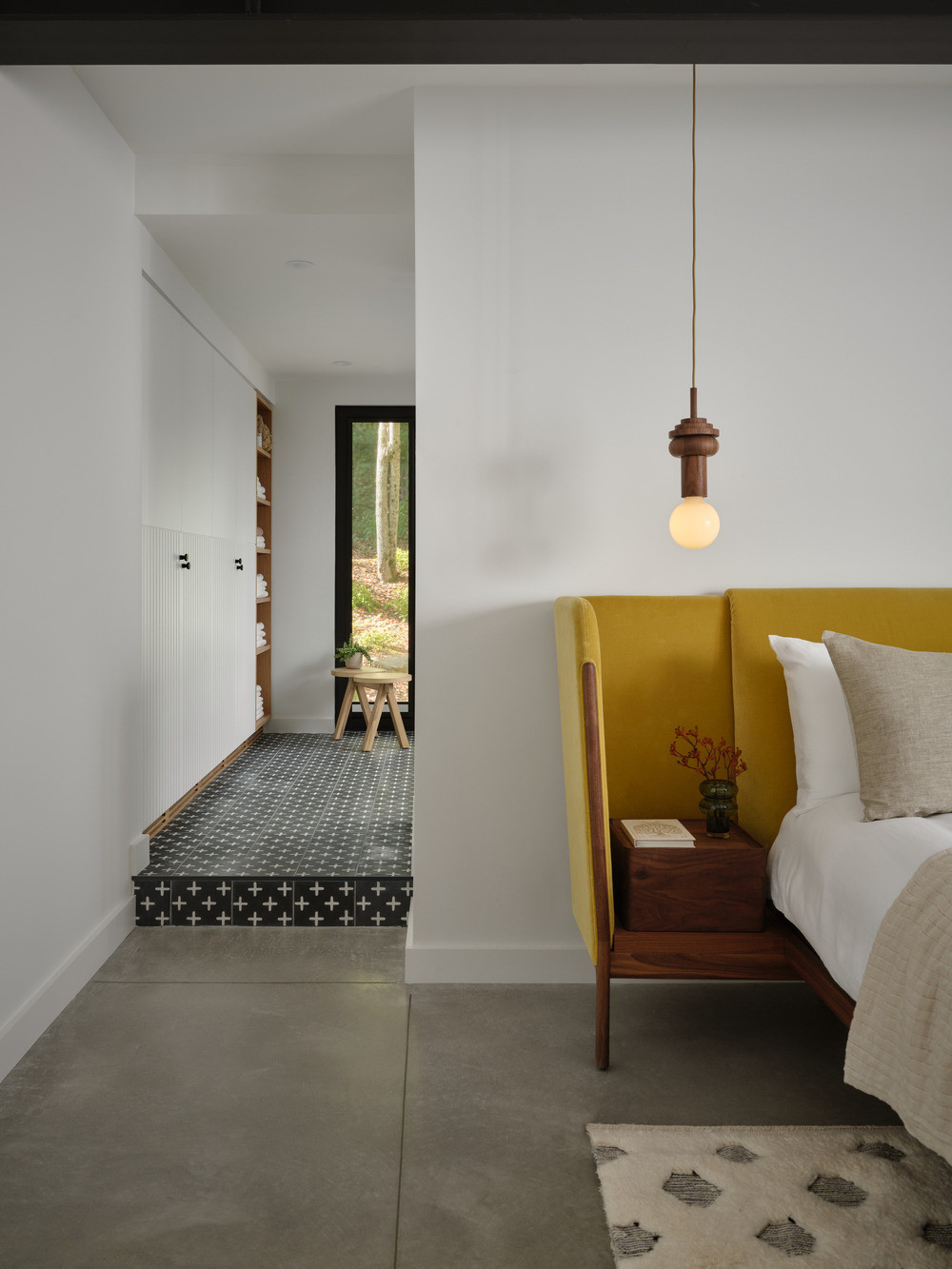 The primary bedroom on the lower ground level has heated poured concrete floors and a mustard-upholstered bed frame
