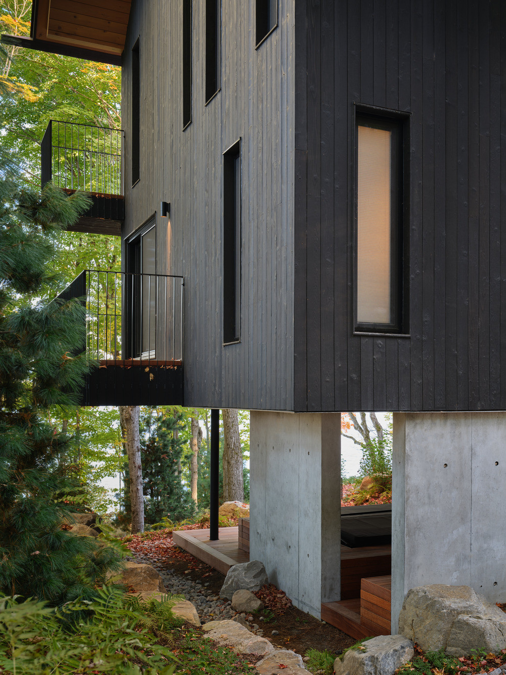 The lake-side elevation, showing stacked balconies serving the upper-level bedrooms, and the concrete structural base at grade