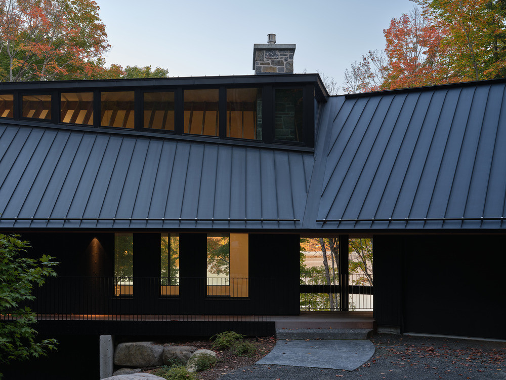 The entry elevation at dusk, showing the clerestory windows where the zinc roof peels back, and the stone chimney above