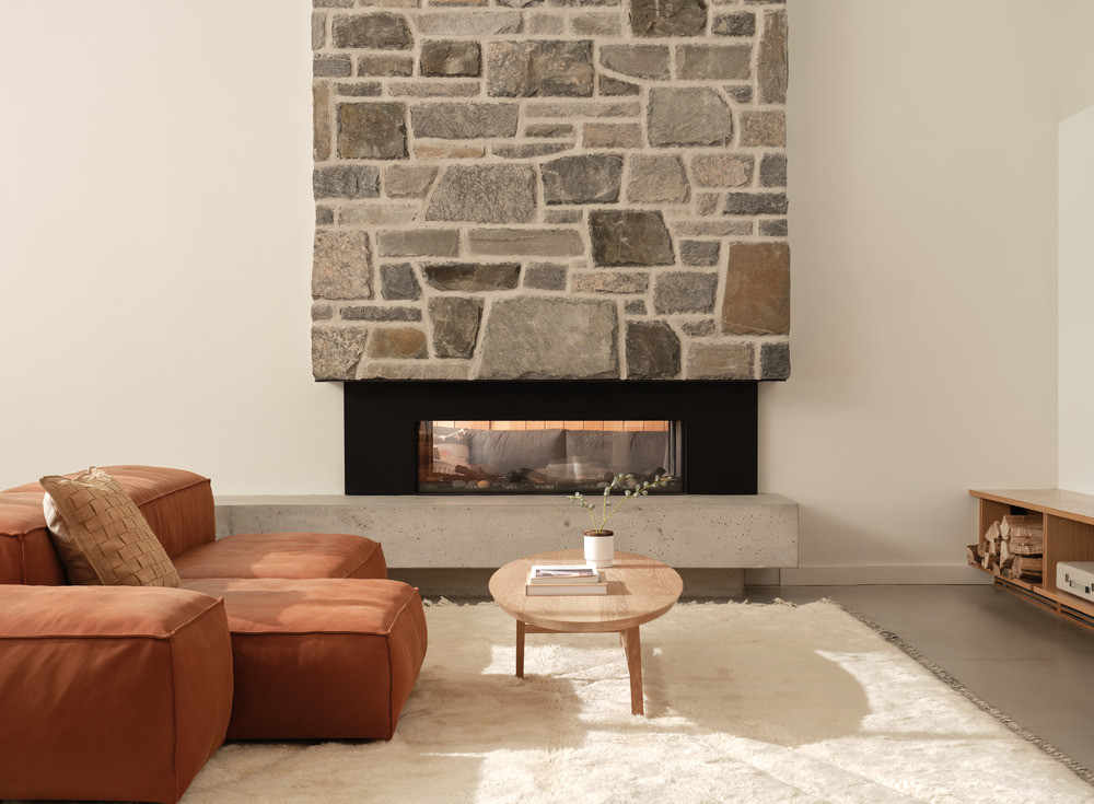 The double-sided stone fireplace on the lower ground level has a poured concrete hearth and the chimney rising through the full height of the structure