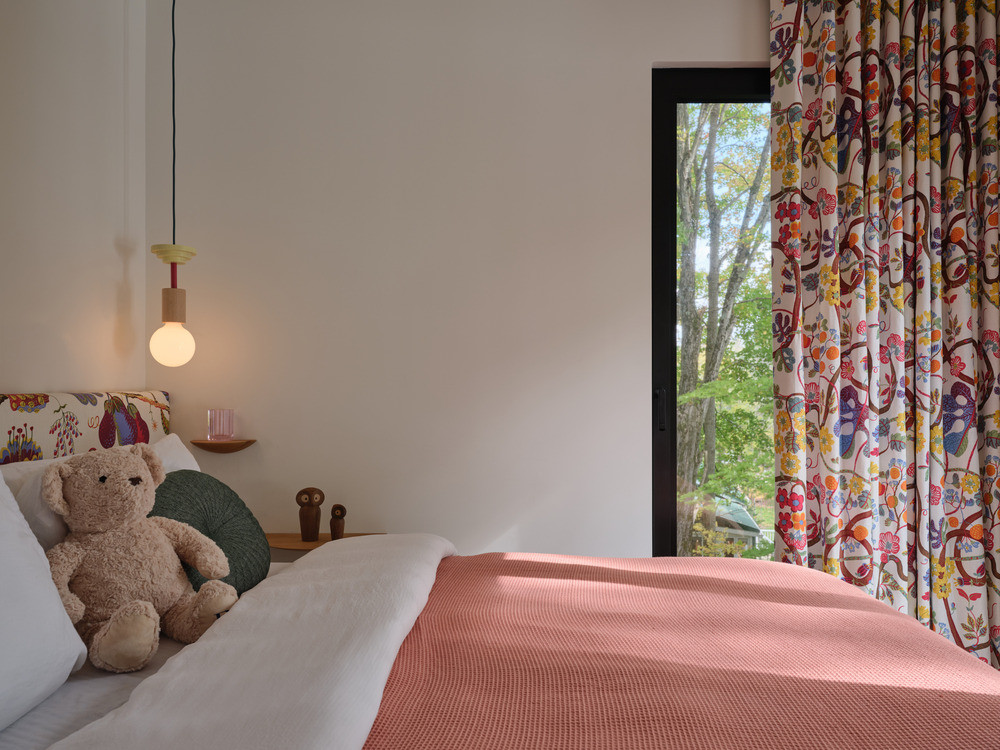 One of the children’s bedrooms on the upper level, with floral curtains and a view into the tree canopy through the bedroom’s full-height window