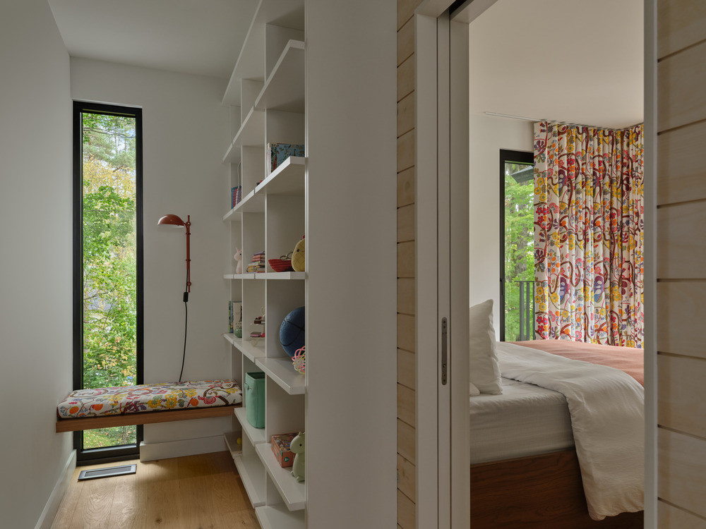 A children’s bedroom on the upper level, with built-in shelving and a window seat overlooking the maple grove