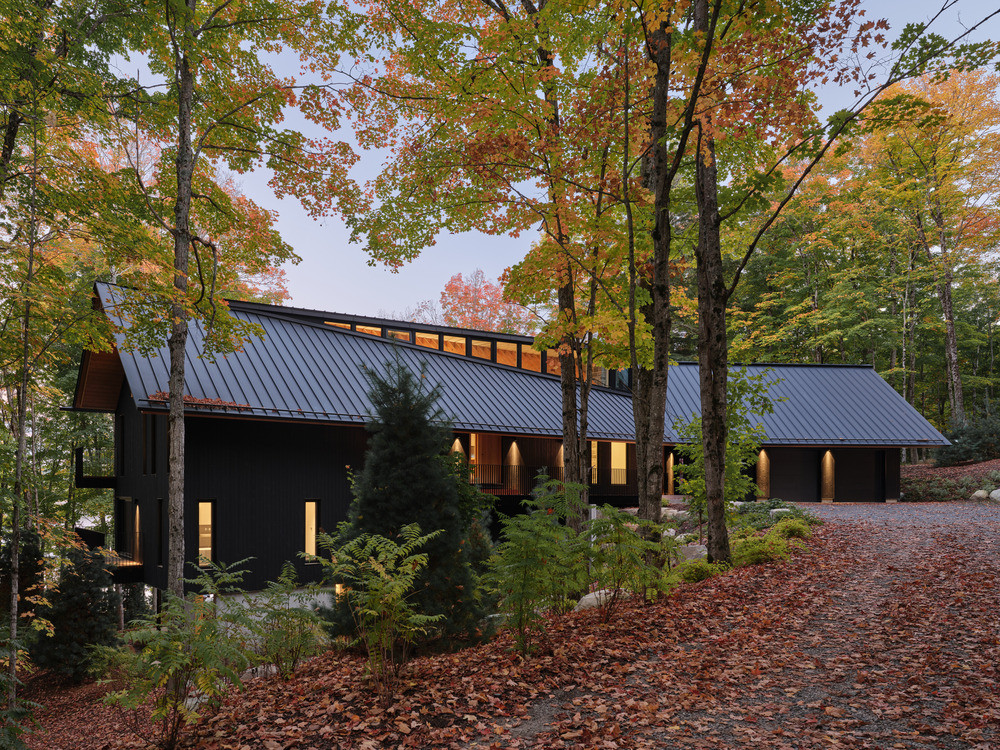 The driveway approach at dusk, with both cedar-clad volumes — the main residence to the left and the garage to the right — visible under their shared black zinc roof
