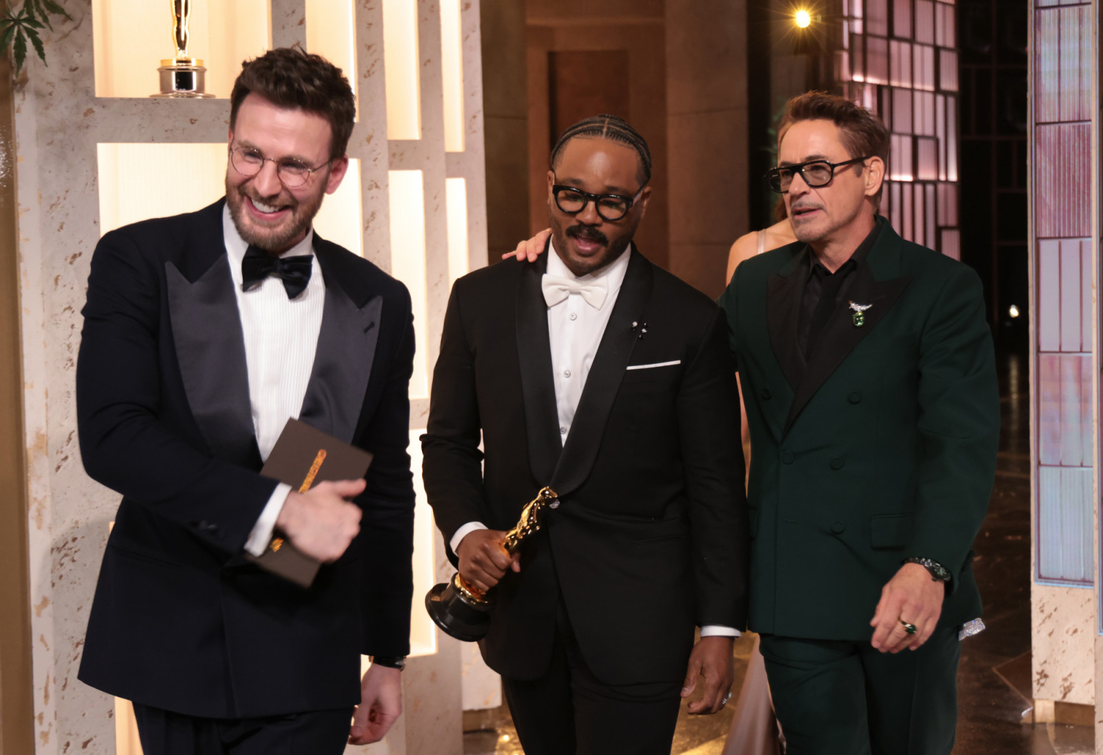 HOLLYWOOD, CALIFORNIA - MARCH 15: In this handout photo provided by The Academy, presenters Chris Evans (L) and Robert Downey Jr. (R) walk off stage as Ryan Coogler carries the Writing (Original Screenplay) award for "Sinners" during the 98th Oscars at Dolby Theatre on March 15, 2026 in Hollywood, California. (Photo by Al Seib / The Academy via Getty Images)