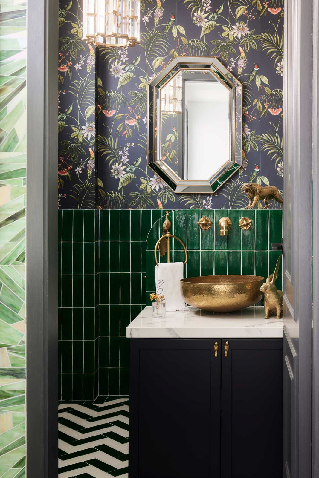 Patterned wallpaper is paired with deep green mosaic tiles, creating a layered and expressive focal point in the powder room