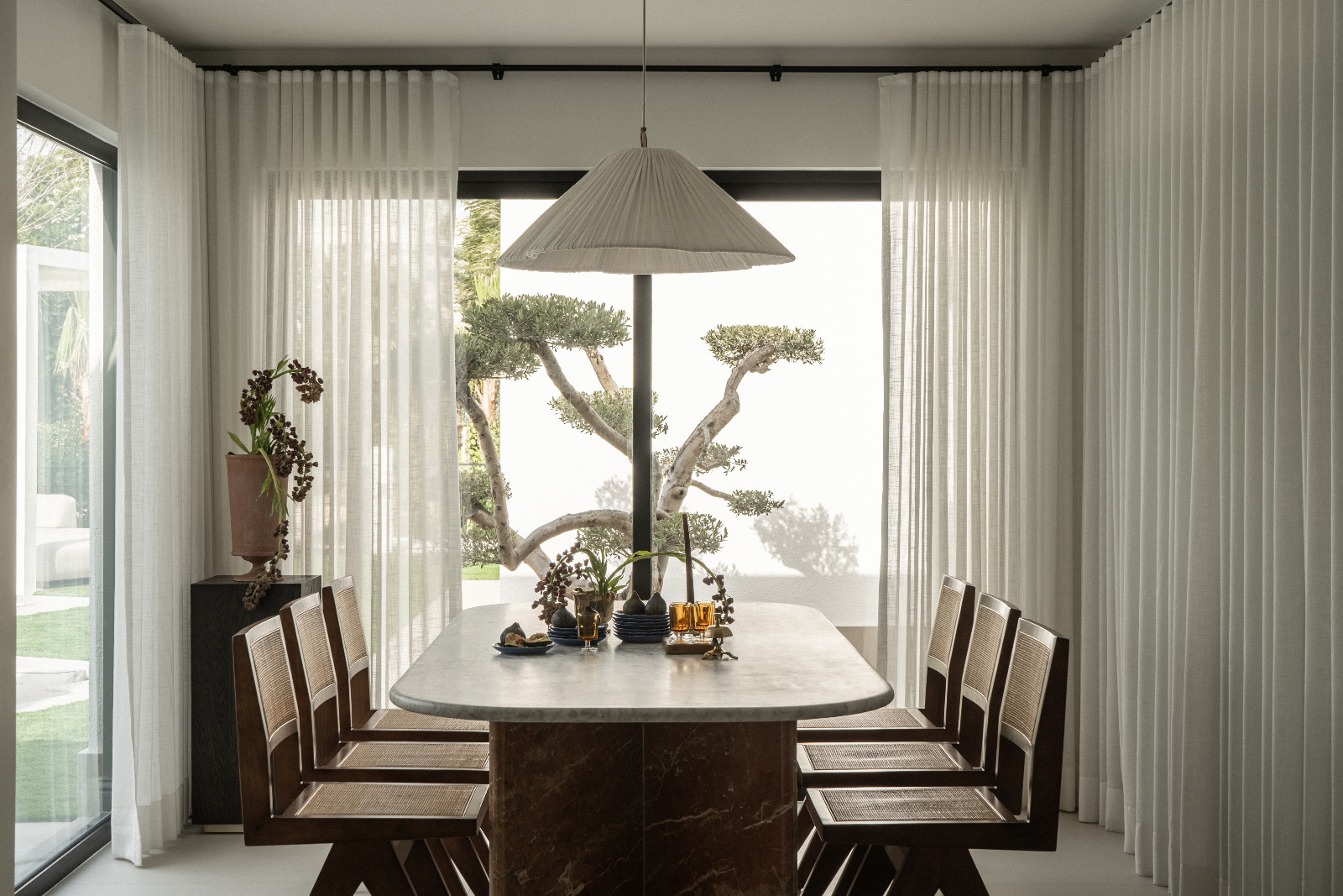 A dining room with views of the garden and bonsai tree in a Dubai family home designed by Amna Chaudry Interiors