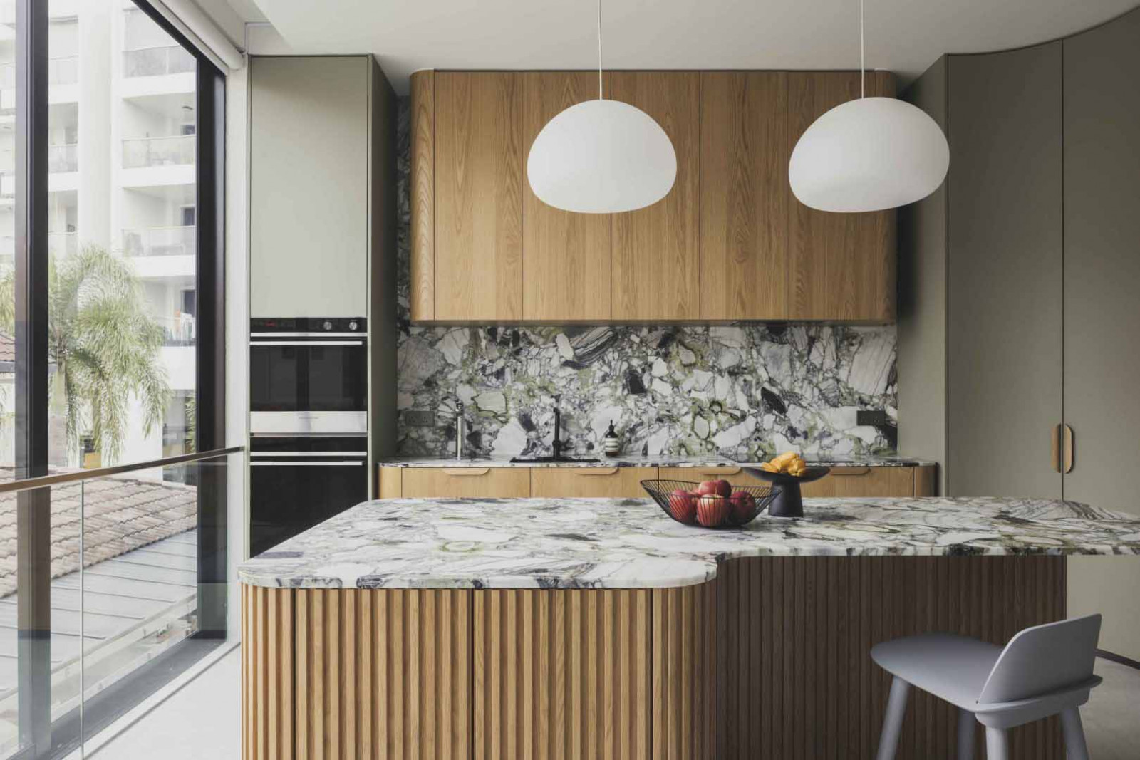 The island doubles as a breakfast counter, defined by fluted timber detailing and a continuous marble surface