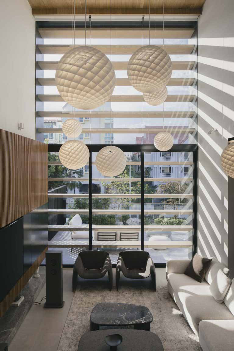 Double-volume living room with external screens filtering light, casting graphic shadows across the semi-detached house’s interiors