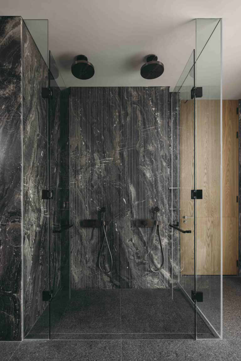 The shower area is enclosed in glass, set against a textured stone wall with vertical striations