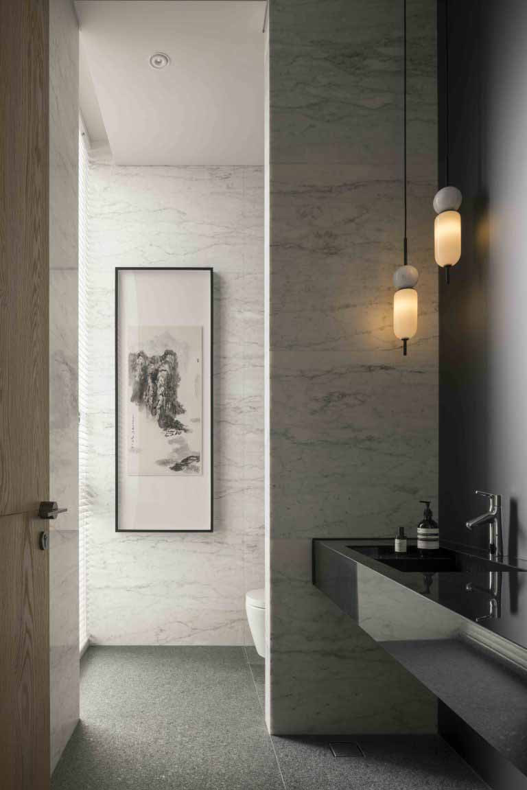 A stone vanity contrasts with darker finishes, accompanied by pendant lighting and framed artwork
