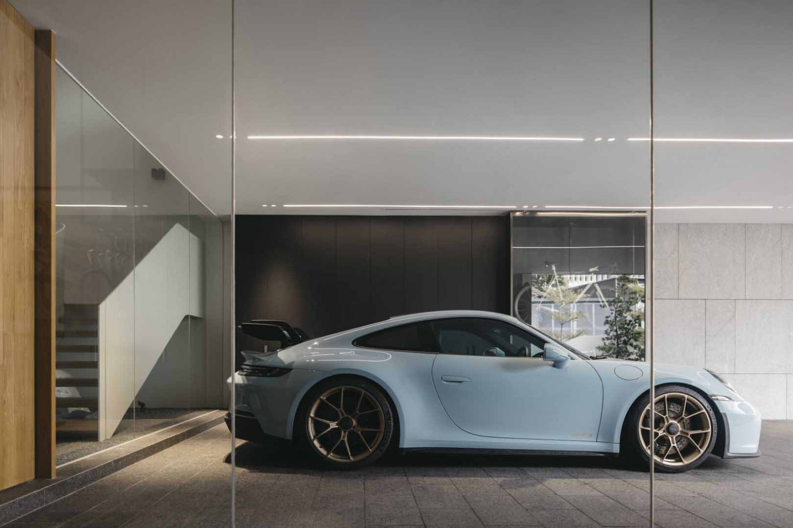 The garage is visually connected to the interior through full-height glazing, with a Porsche on display