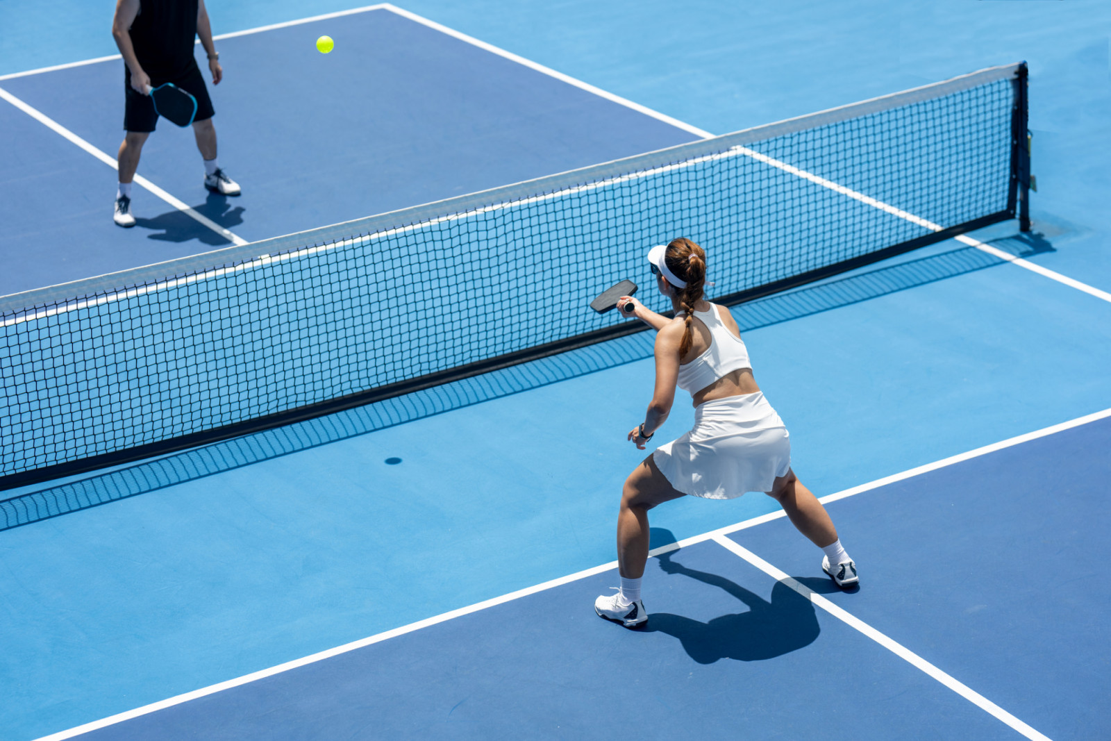 A female pickleball player returns a serve of a bright yellow ball on a dedicated court at a public park.