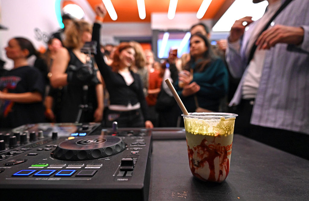 PRODUCTION - 17 January 2026, Berlin: A plastic cup filled with matcha latte stands next to a DJ booth. Dancing young people can be seen in the background. At the "Coffee Rave" event, partygoers in Berlin can dance to electronic music in the morning. Only non-alcoholic drinks are sold in the café. According to the organizer, many young people are looking for party alternatives in order to celebrate in a healthy way. Photo: Elisa Schu/dpa (Photo by Elisa Schu/picture alliance via Getty Images)