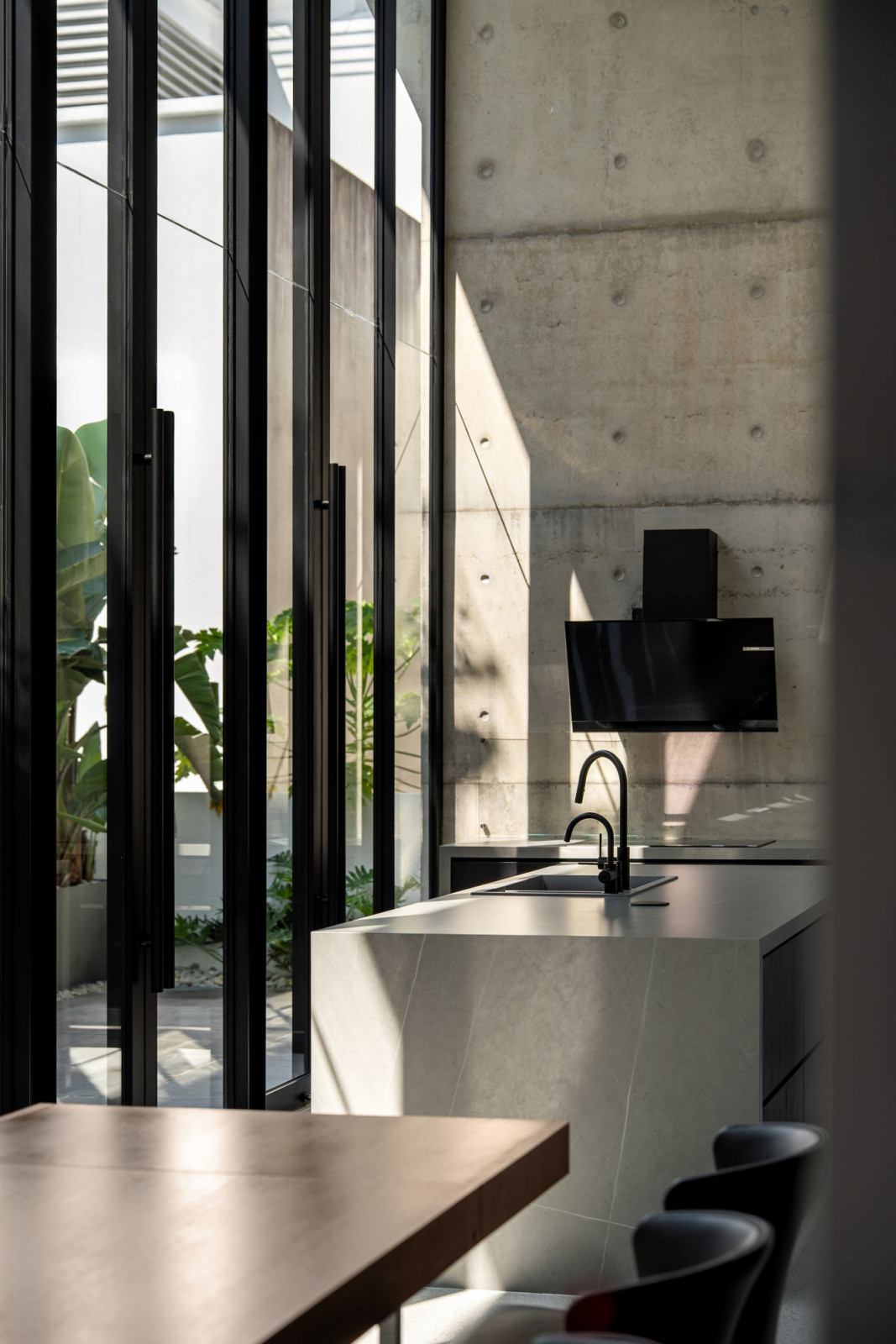 The wet kitchen sink and range hood against the raw off-form concrete wall, with the garden visible through the closed glass panels
