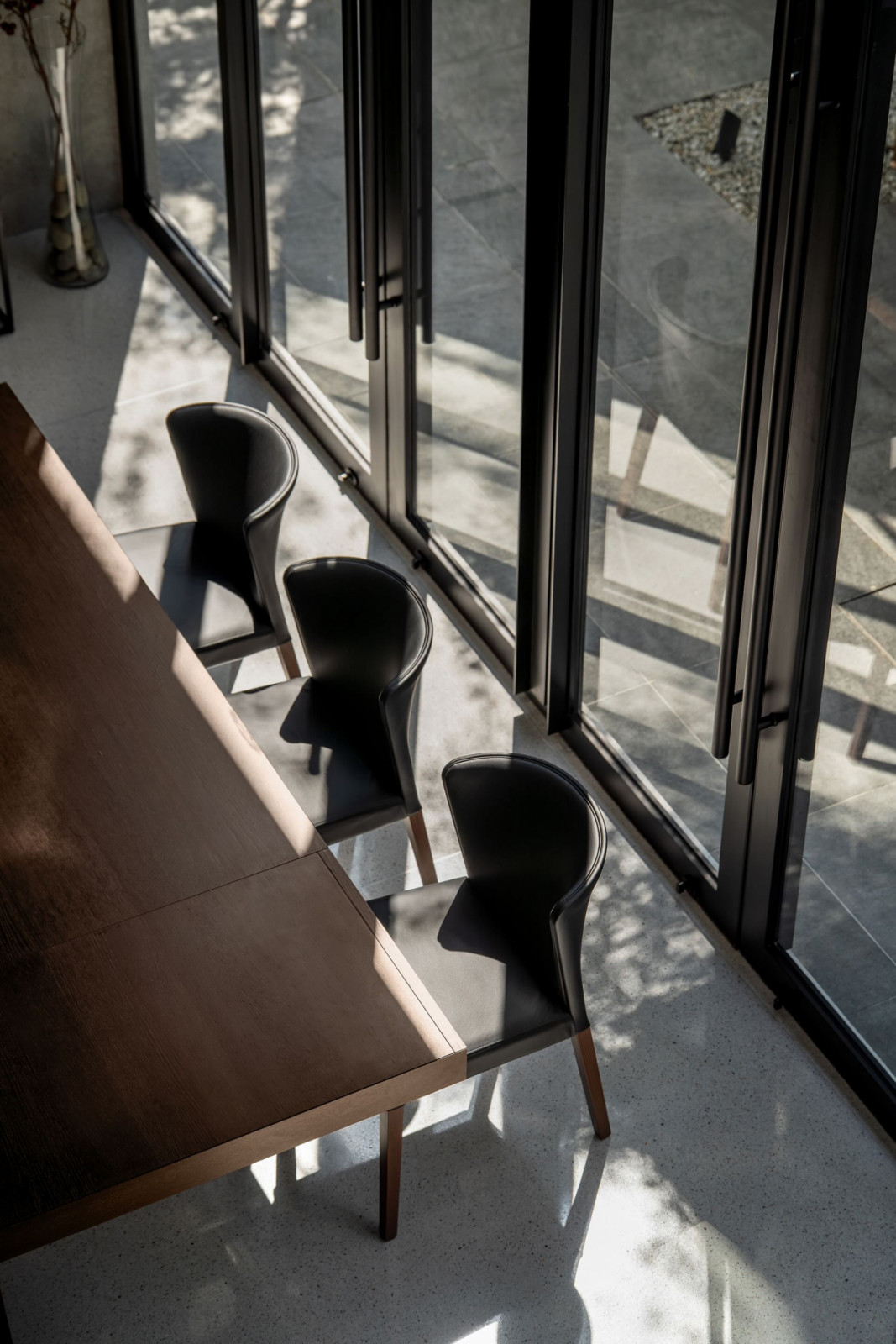 The dining chairs and timber table seen from above, with the pivoting glass panels and garden floor beyond