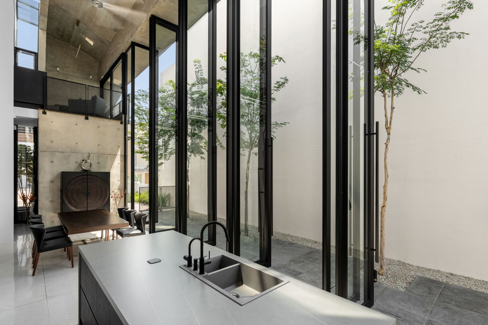 The full length of the wet kitchen and dining hall, with garden trees visible through the closed glass panels