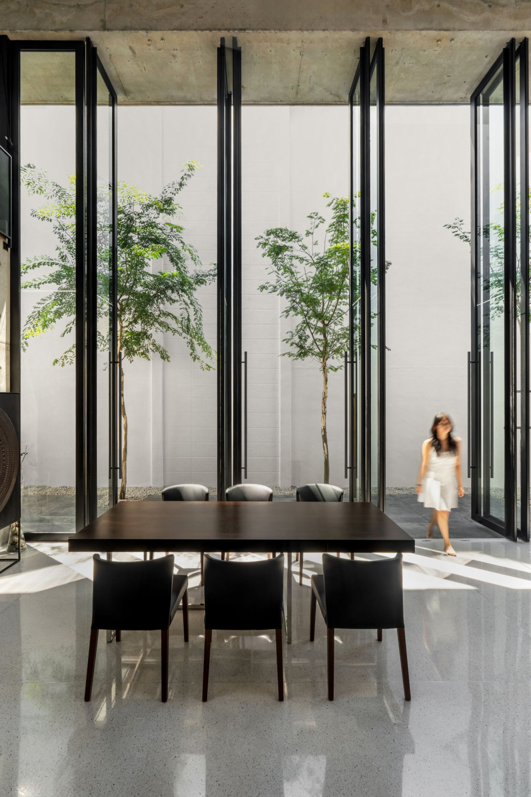 The dining hall has the glass panels partially open, and trees planted along the garden edge are framed within the black steel mullions