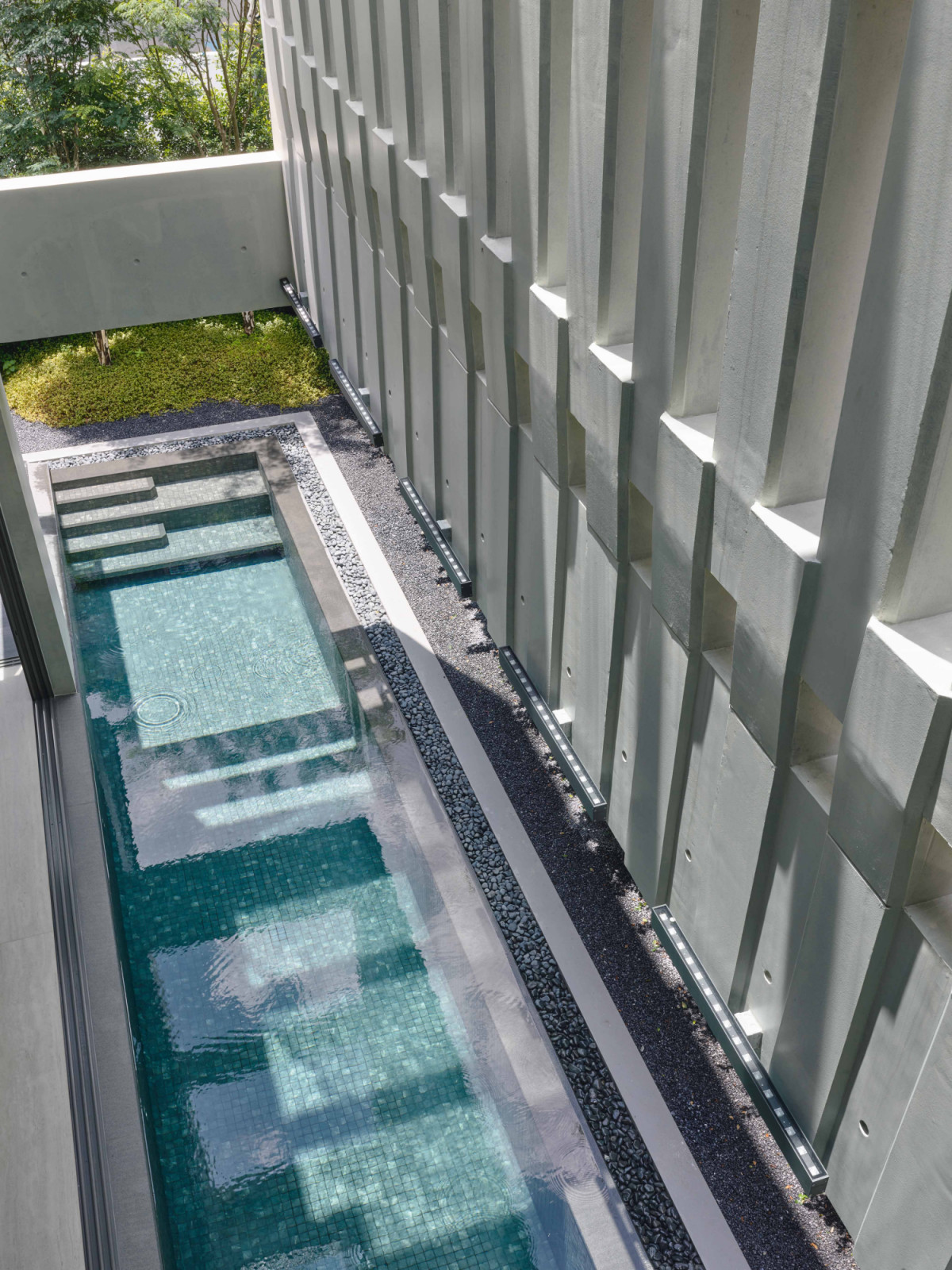 The terrace house’s concrete structure casts poetic shadows over the swimming pool