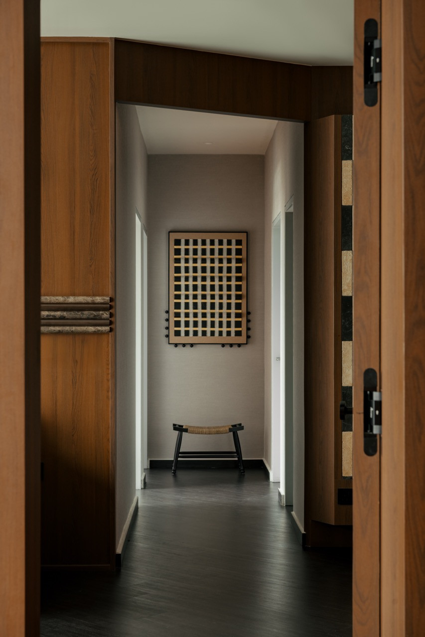 A view through the timber-framed entrance into the corridor, where a small woven stool sits below a framed grid artwork at the far end
