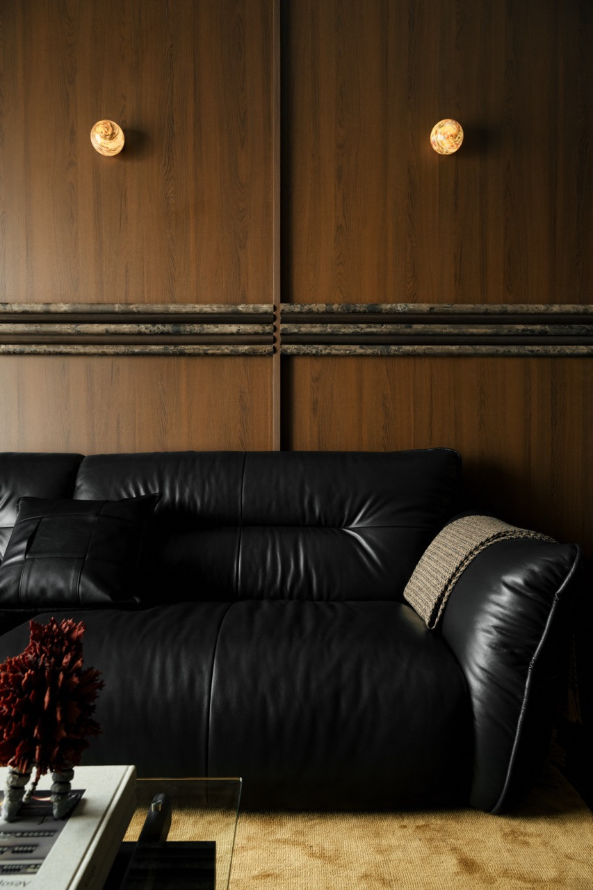 Detail of the timber feature wall behind the sofa, with two amber swirl glass globe sconces and a horizontal run of dark stone moulding dividing the panels