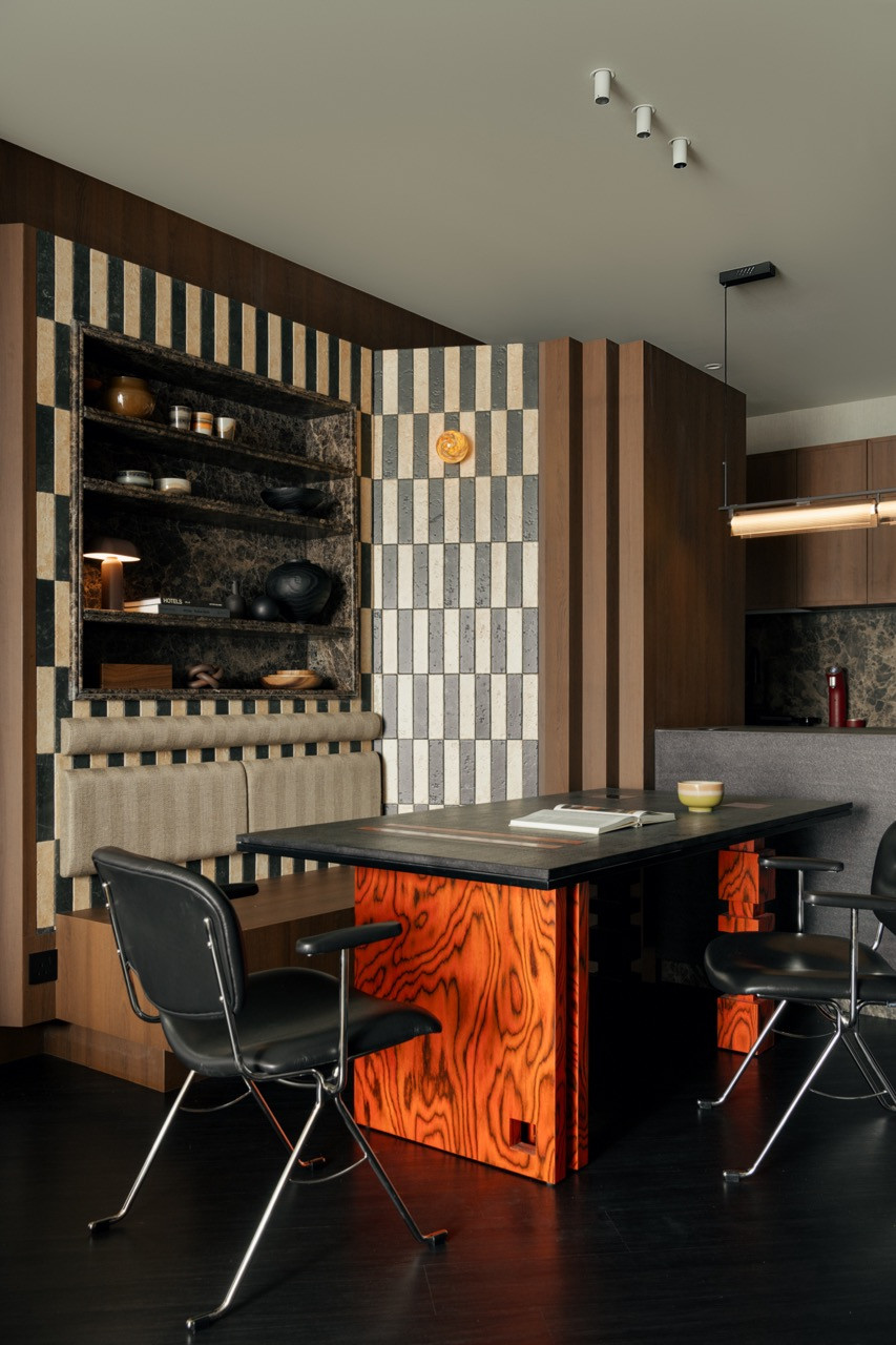 The dining area, with the black stone table on sculptural red-orange figured wood legs, faces the dark marble display niche framed in cream and slate tiles