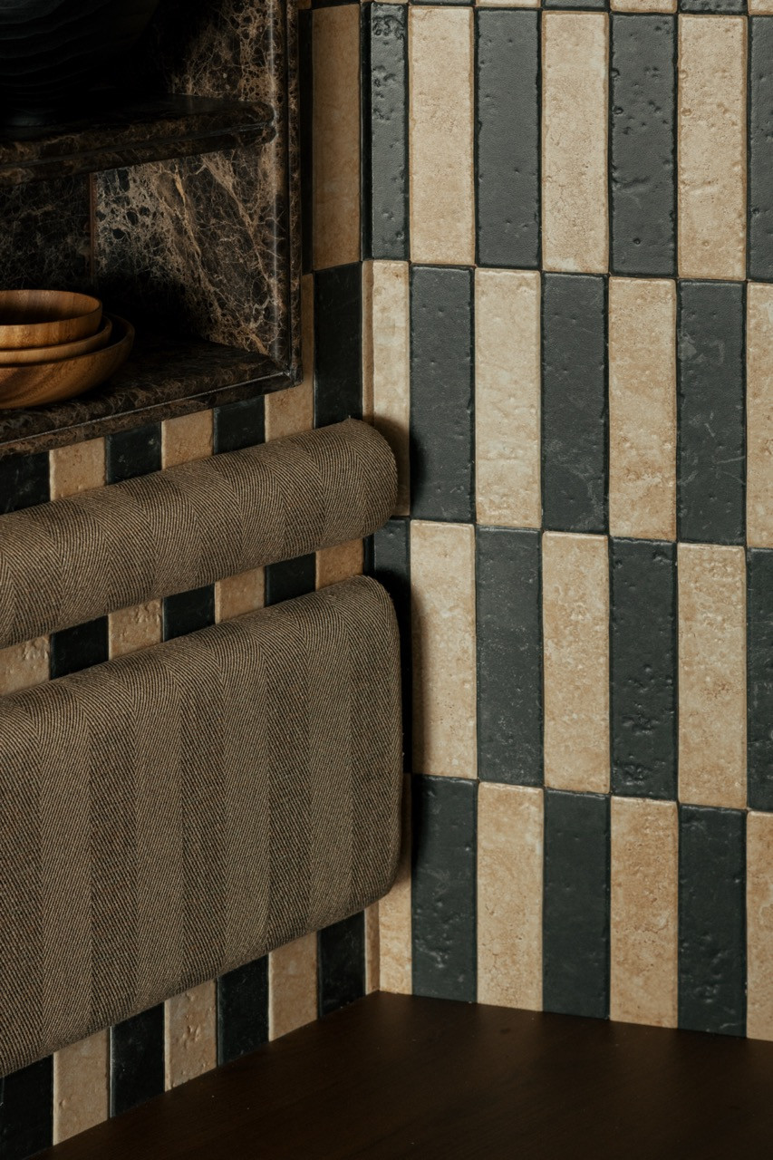 The full display niche is set into the checker-stripe tiled wall, with an amber glass wall sconce and a woven bolster bench below