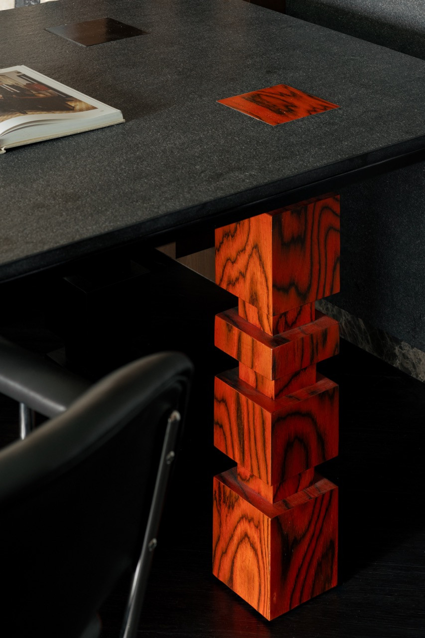The dining area looks towards the corridor, with the tiled display niche anchoring the wall and the red-orange wood table base visible in the foreground