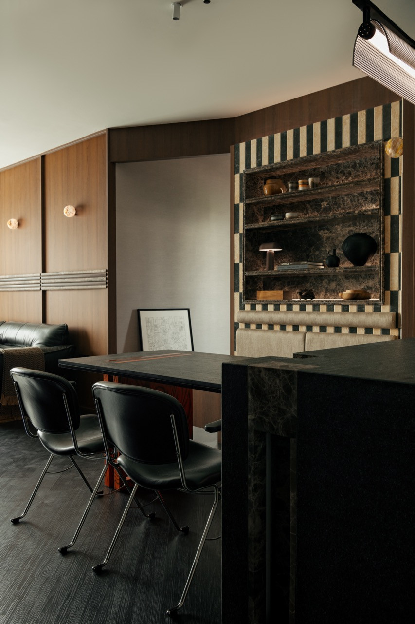 A wide view of the dining and kitchen zone, with the checker-tiled feature wall, black leather chairs and copper tube pendant overhead